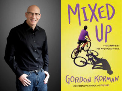 Gordon Korman standing next to his book called Mixed Up. Book cover shows a boy on a bicycle.