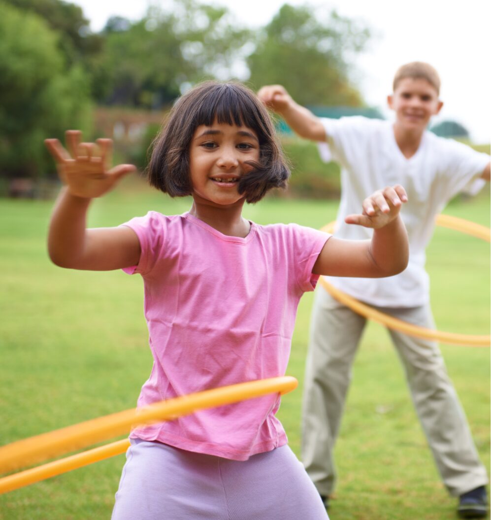 shows a girl hula hooping outside on the grass.