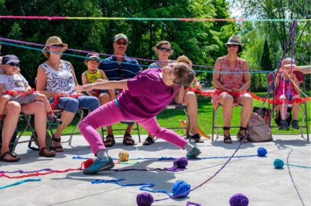 photo of a woman doing the limbo under a colourful string of yarn in front of an audience.