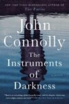 Book cover of The Instruments of Darkness by John Connolly shows the mirrored reflection of a person standing over a puddle of water. 
