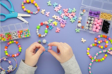 Photograph of a child's hands stringing a coloured bead on to a string. The child is surrounded with different coloured beads, a and pair of scissors and a few many-coloured beaded child's bracelets.